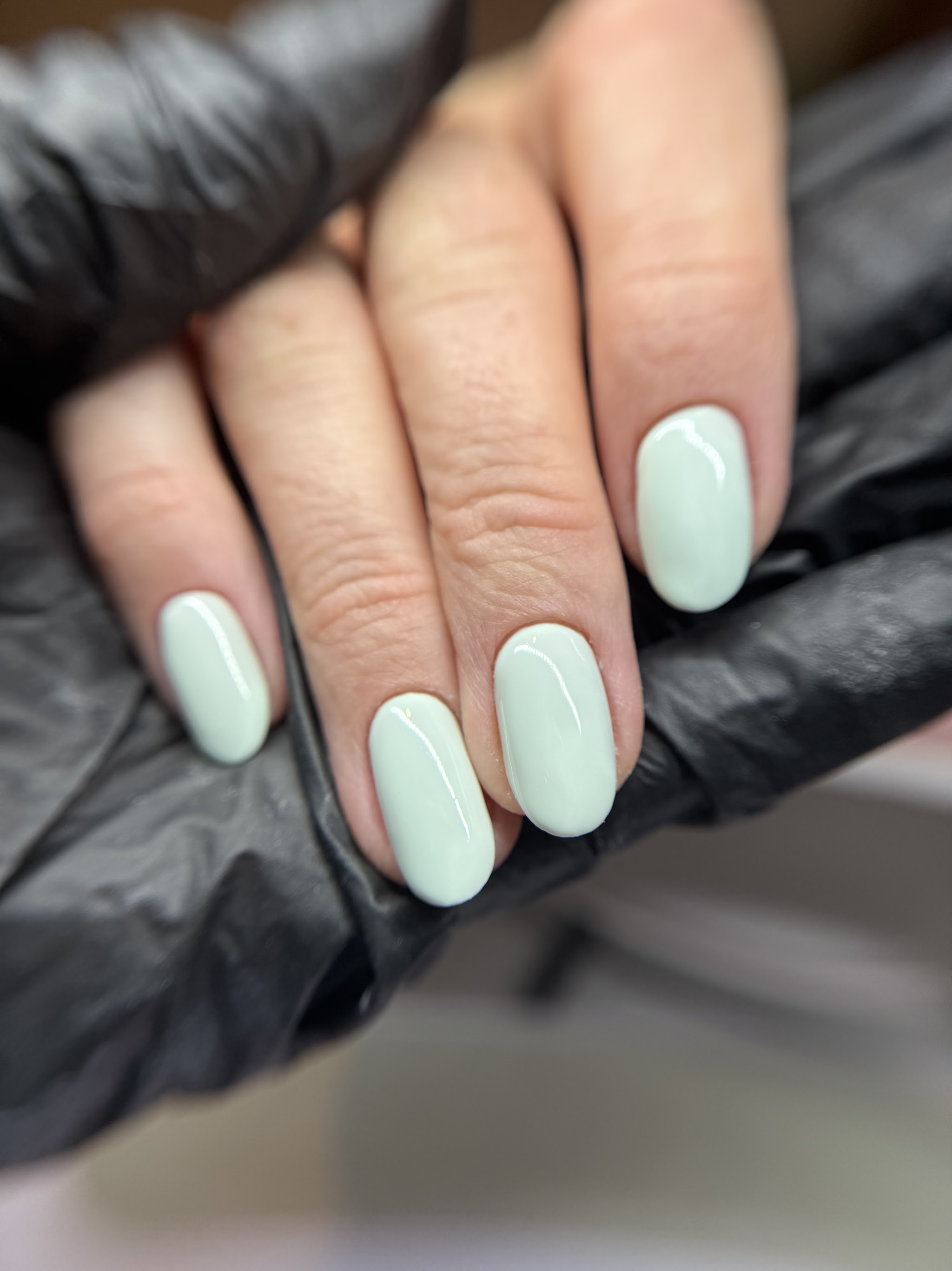 Mintgroene ovale gelnagels, vastgehouden met een zwarte handschoen